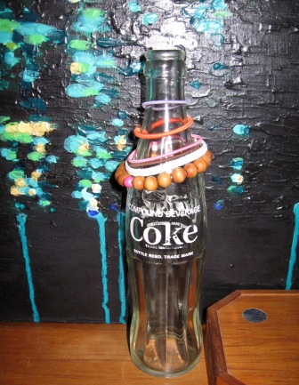 Old coke bottle used to keep hair ties at the ready with a painting by Alex Di Mecurio in the background